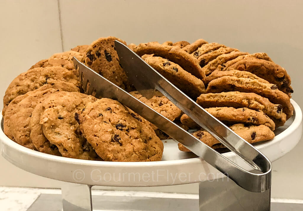 A tray of oatmeal raisin cookies are placed on a platter with a pair of tongs.