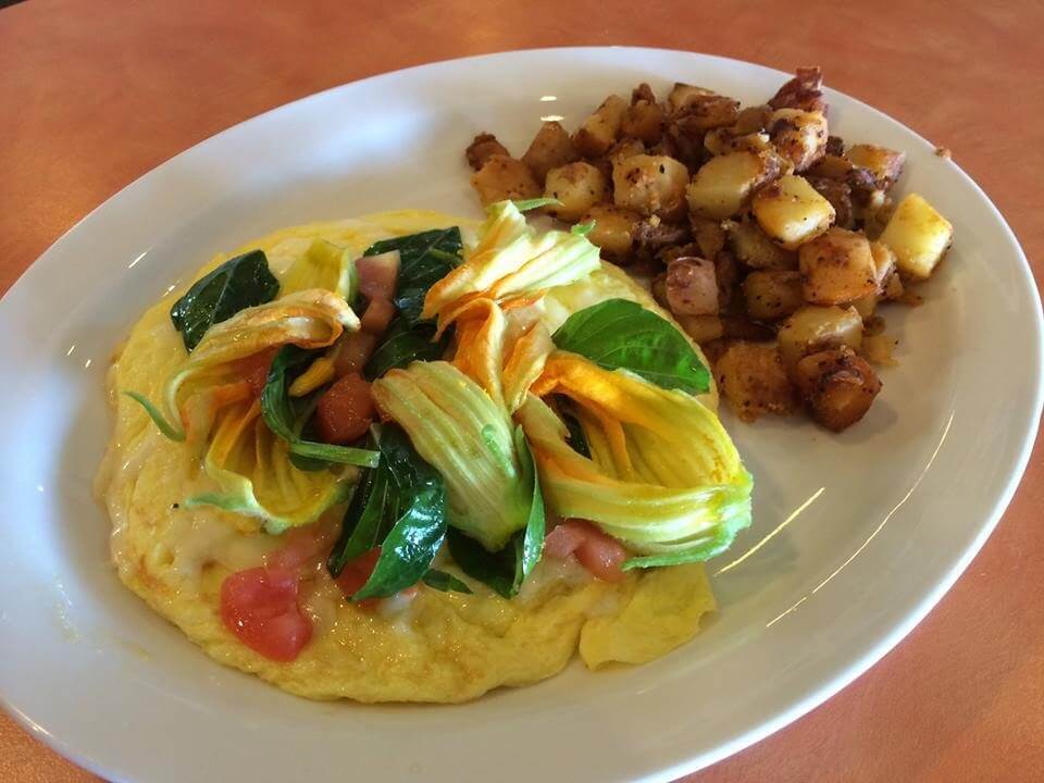 A circular omelet topped with diced tomatoes and green vegetables is served with a side of fried diced potatoes.
