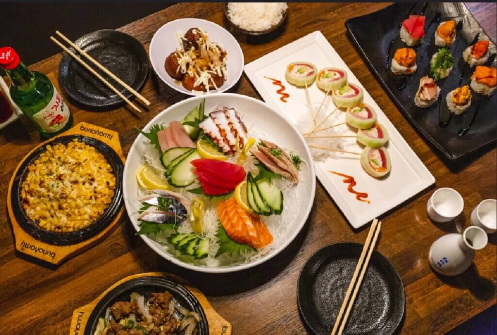 Colorful Japanese food like sushi, sashimi, and some hot plate dishes fill a tabletop.