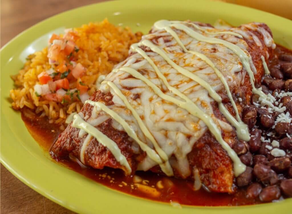 A plate of beef enchilada topped with melted cheese and served with beans and salsa on the side.