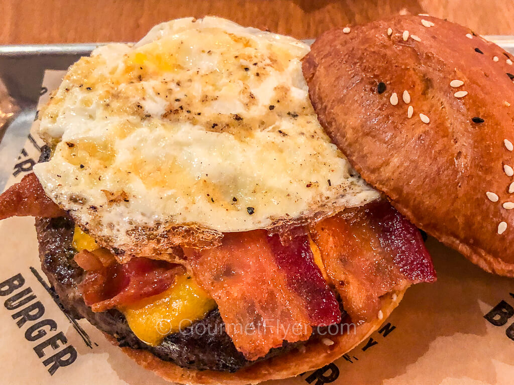 A burger with its crown slid open shows the toppings of cheese, bacon, and a fried egg.