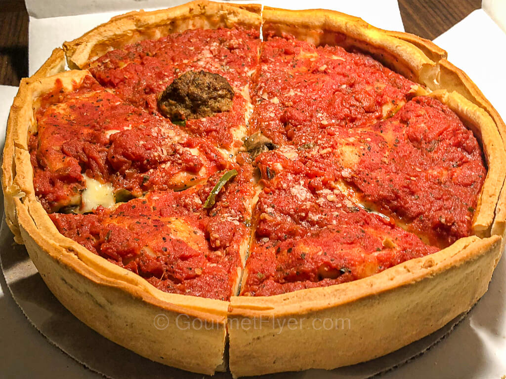 A Chicago deep dish pizza with a tall edge is topped with tomato sauce.