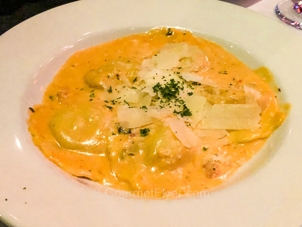 A dish with ravioli drenched in a yellow creamy vodka sauce.