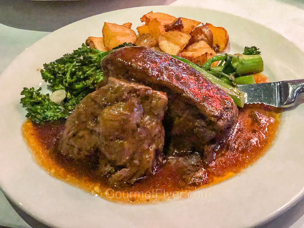 A plate of beef ribs served with long broccolini and diced potatoes.