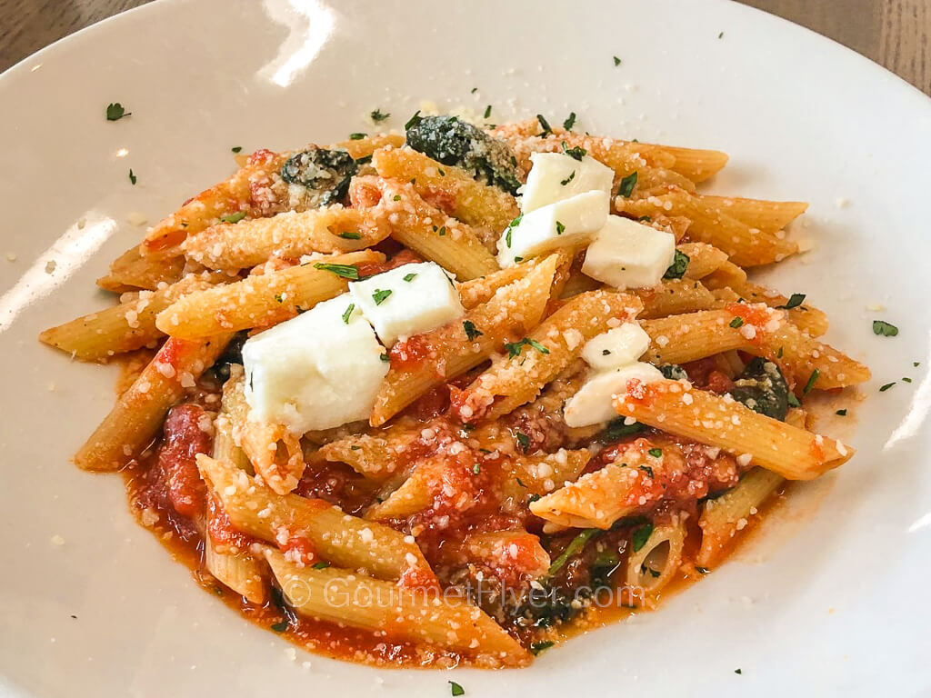 A dish of penne pasta with tomato sauce, spinach, and cubes of fresh mozzarella cheese.