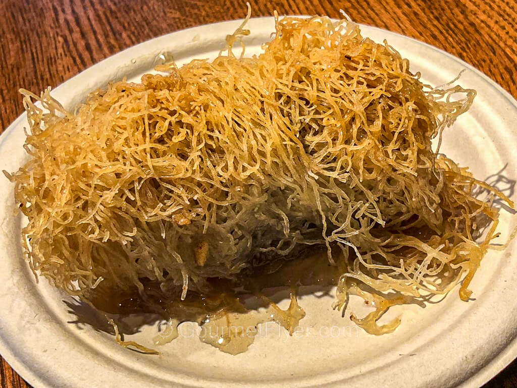 A pastry with a thin noodle-like shell is served on a white paper plate.