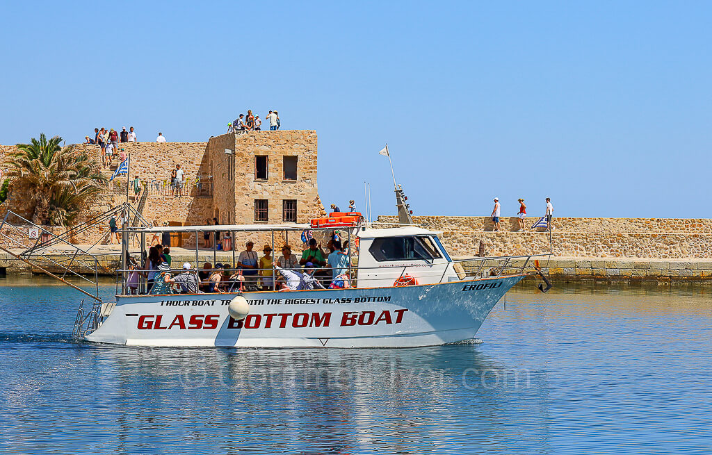 A small boat labeled Glass Bottom Boat carries a couple dozen passengers with a fortress in the backdrop.