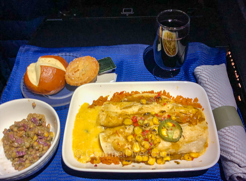 A plate of cheese enchiladas is served with a side salad, bread, and a pie in the sky. A glass of red wine accompanies the tray.