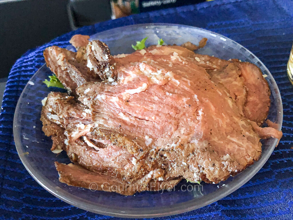 Thin slices of slightly pink medium well roast beef are served on a plate.