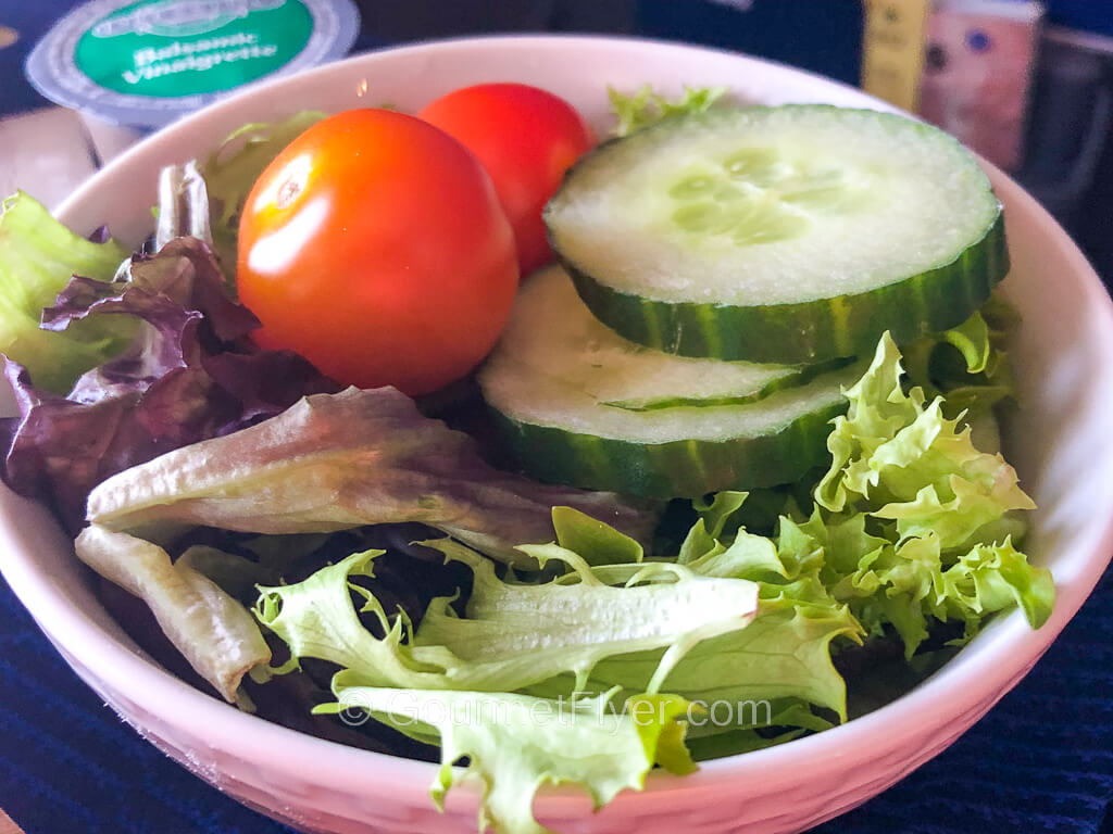 A bowl of green salad is topped with two cherry tomatoes..