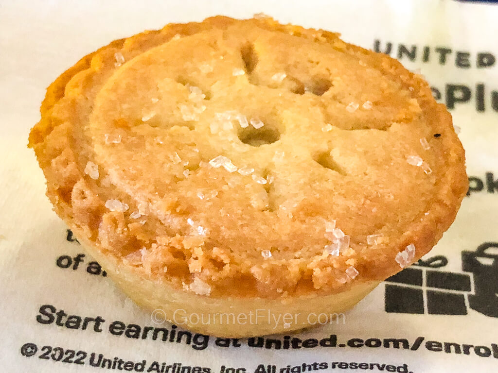 A pie shaped cookie is topped with coarse grains of sugar and served on a United napkin.