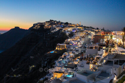 The 3-day Santorini itinerary features the gorgeous island in dusk with orange sky and dimly lit whitewashed houses.