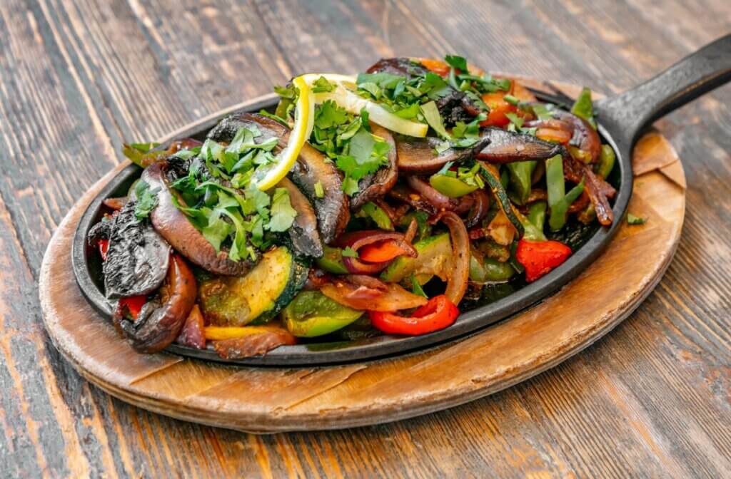 A sizzling platter of fajita is topped with peppers and veggies.