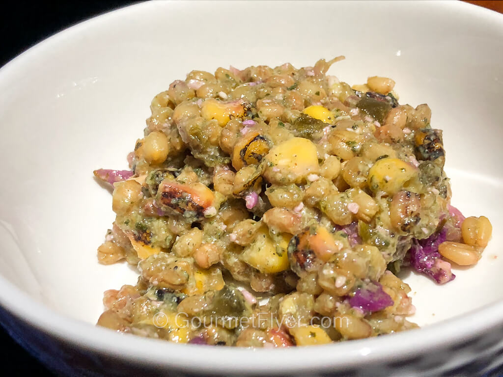 A bowl of grain salad consisting of a blend of wheat berries corn, peppers, and red cabbage.
