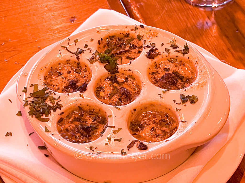 An escargot dish with 6 slots filled with melted garlic butter and escargots.