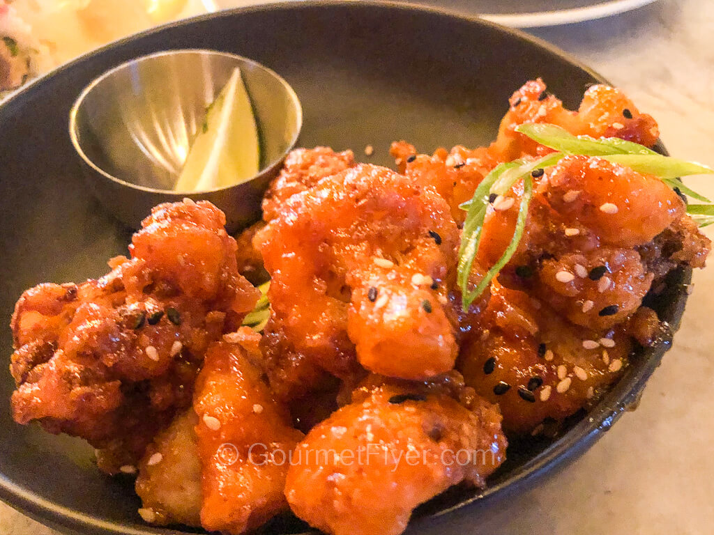 A plate of fried cauliflowers is served with a wedge of lemon.