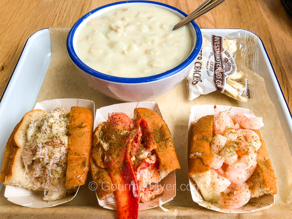 From left to right, crab roll, lobster roll, and shrimp roll, accompanied by a bowl of clam chowder.