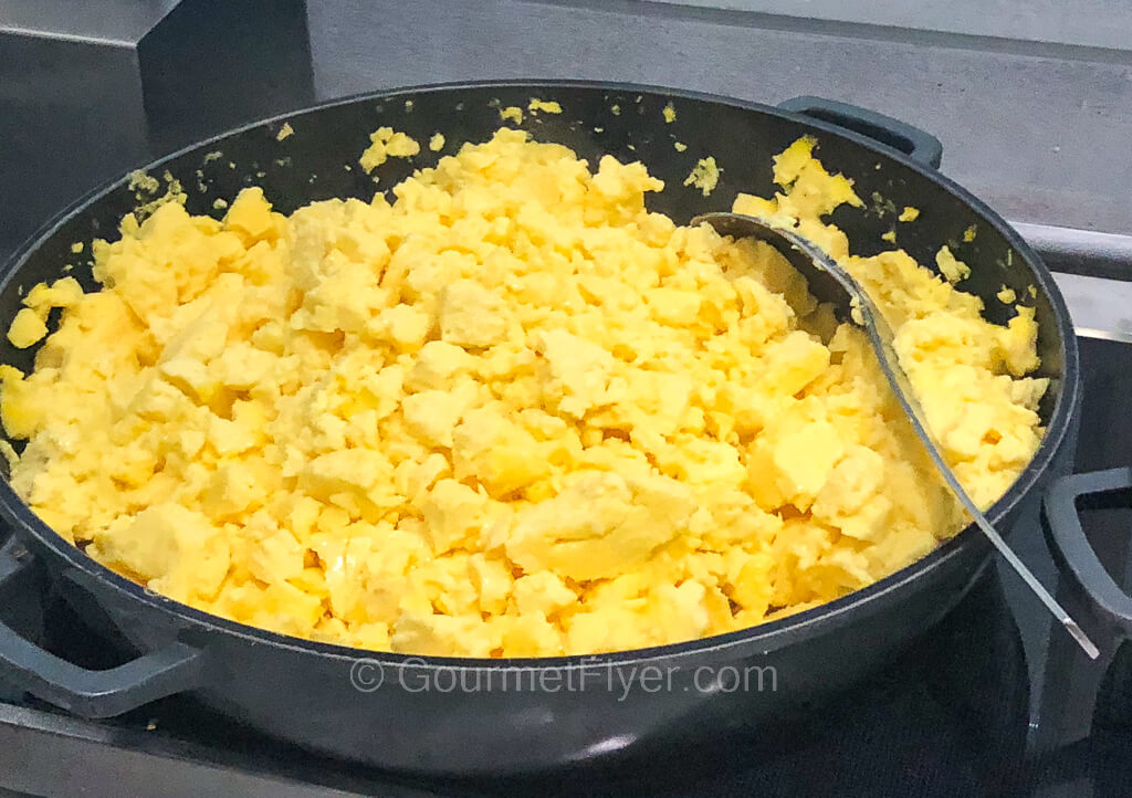A large platter of scrambled eggs with a serving spoon.