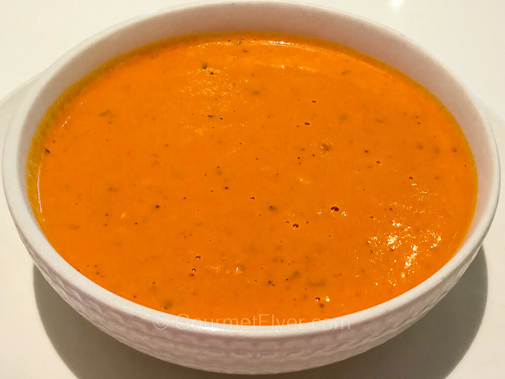A bowl of creamy red soup sits on a serving plate.