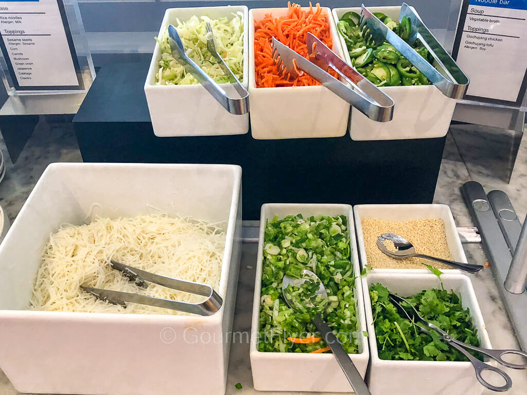 Glass noodles are placed in a container alongside bowls of vegetable toppings.