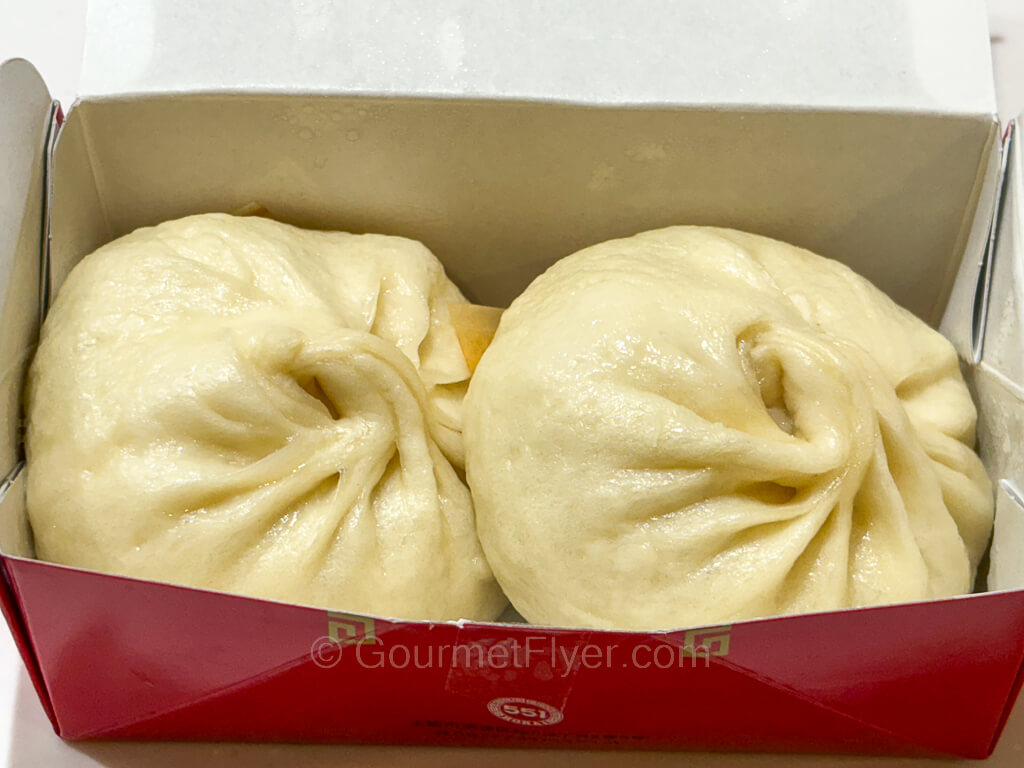 Two Chinese style steamed buns are packed inside a paper box.