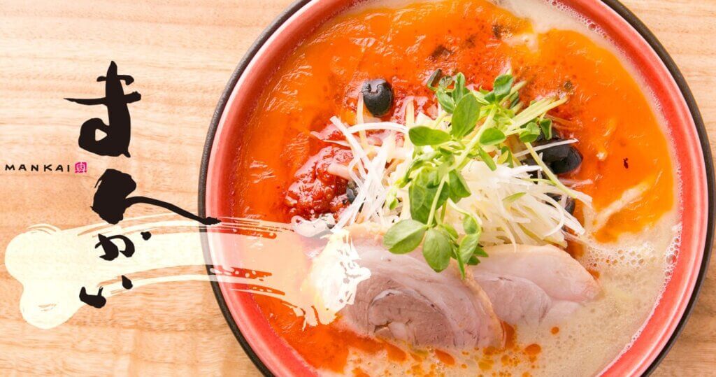 A bowl of ramen in a tomato-based pork bone broth topped with tonkotsu and garnishments.