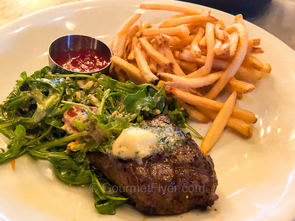 A steak topped with butter is accompanied by a side salad and French fries.