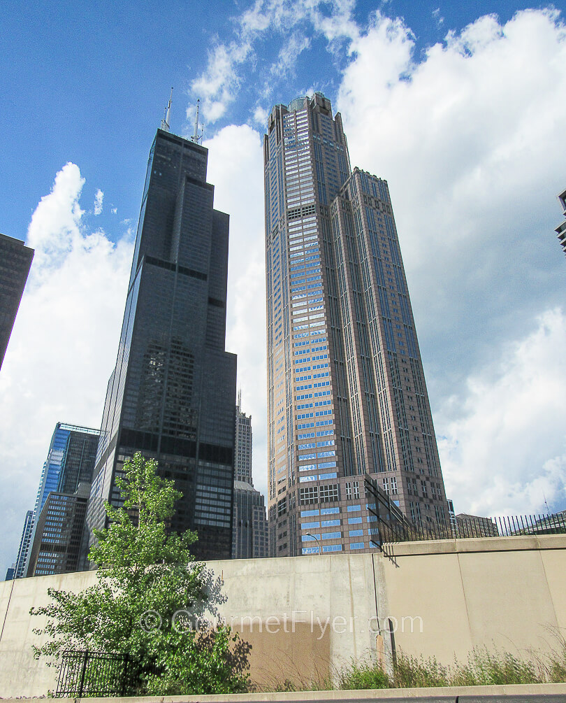 Two skyscrapers point toward a blue sky partially covered with clouds.