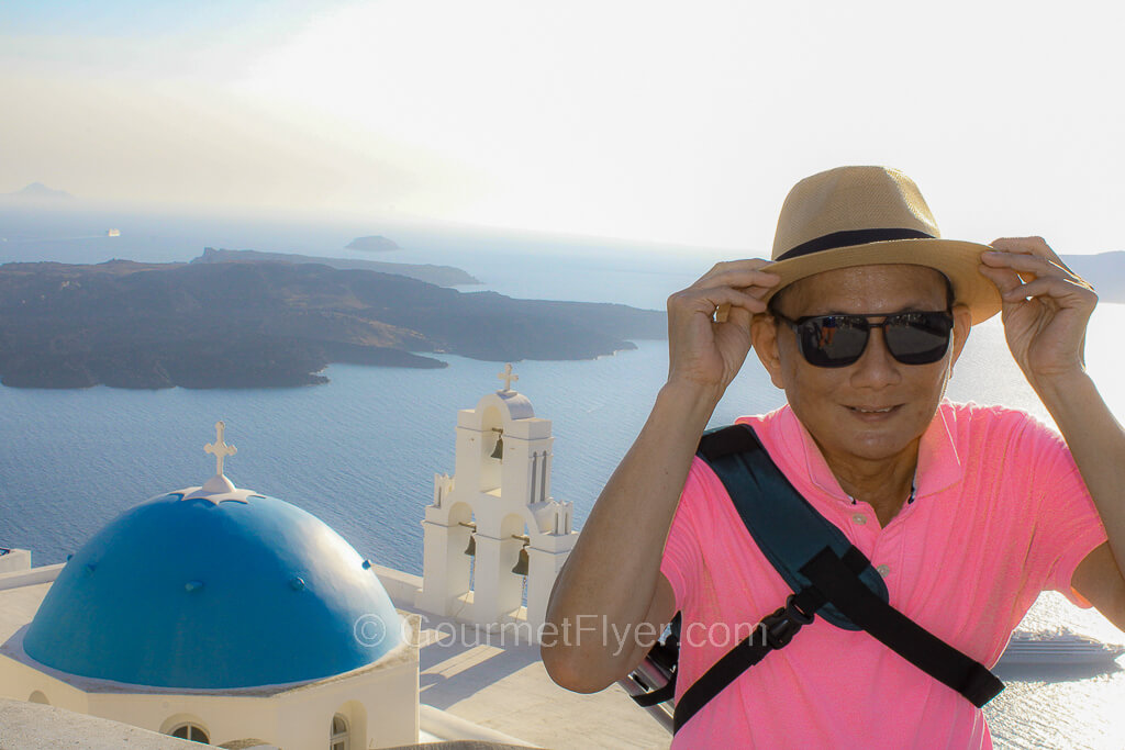 The Gourmet Flyer is posing at the iconic Blue Dome of Santorini.
