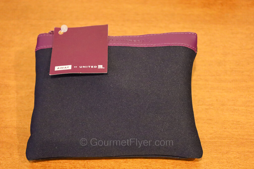 A blue fabric pouch of a premium economy class amenity kit with a United logo tag.