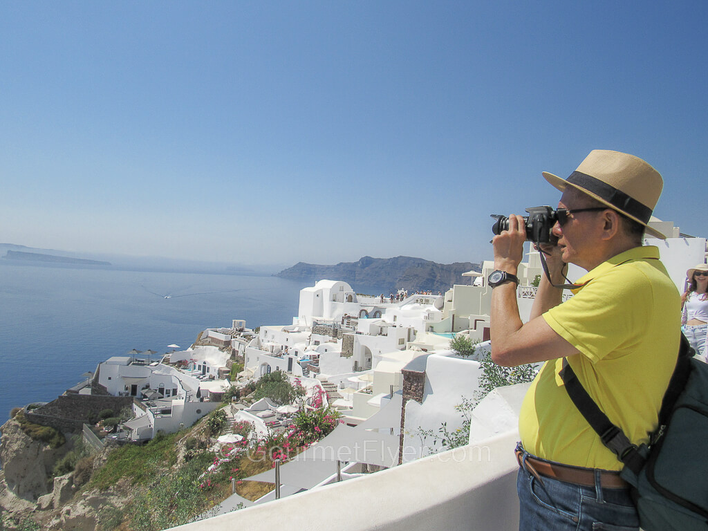 The Gourmet Flyer is taking pictures from the balcony of a restaurant in Oia.