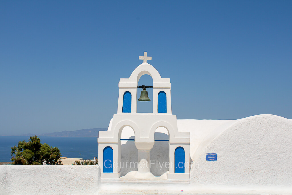 View of a Church with bells with blue doors and whitewashed walls in Oia.