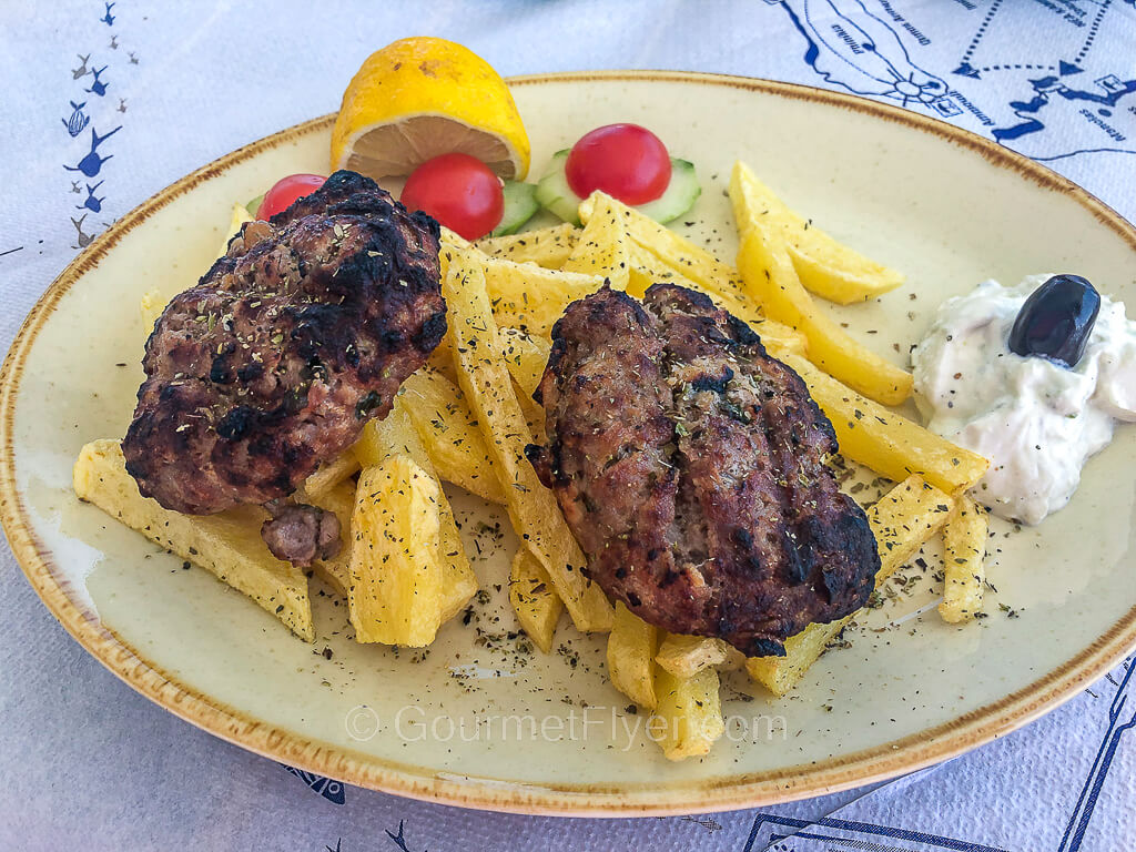 Two hamburger patties are served with French fries and garnished with cherry tomatoes and dusted with parsley.