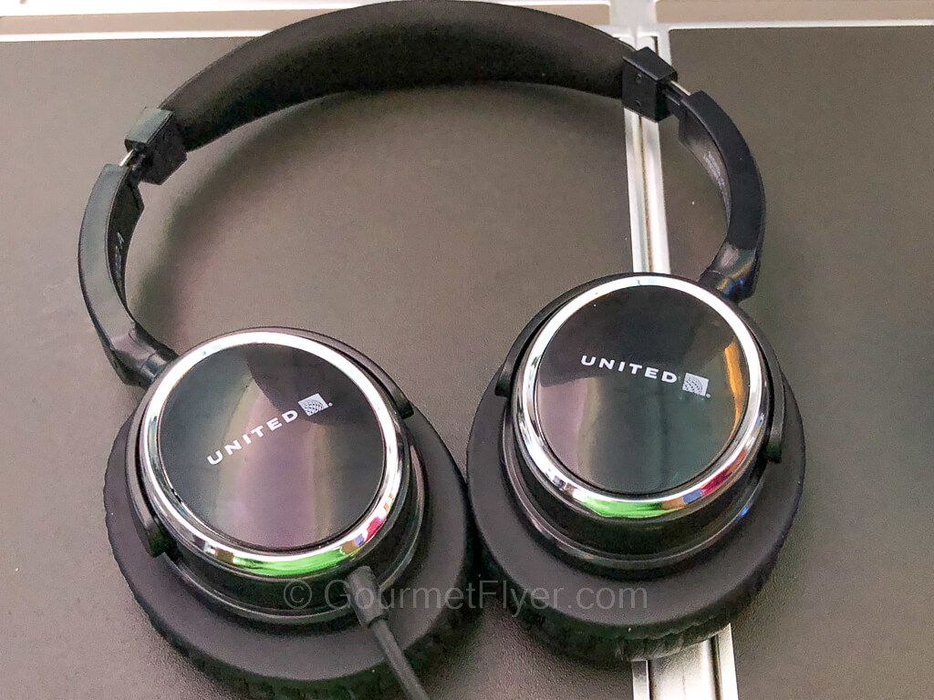 A pair of headphone with United Airlines' logo sits atop the tray table of a seat.