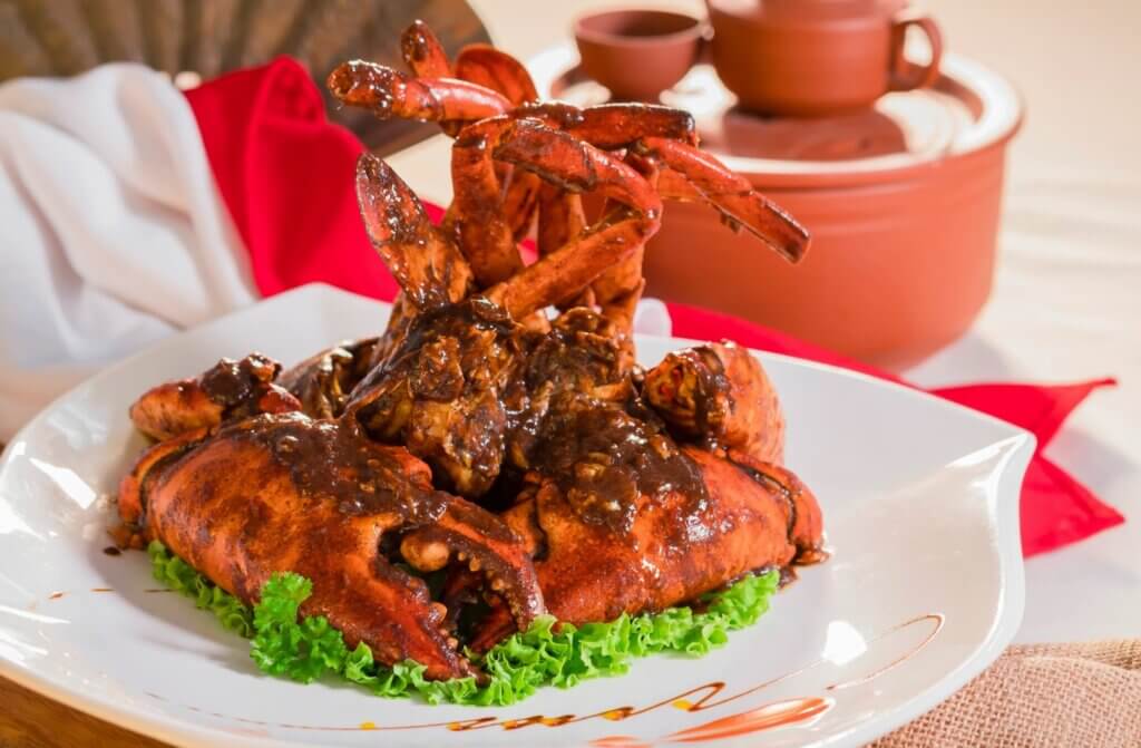 A cooked crab is served with black pepper sauce over a leaf of lettuce.