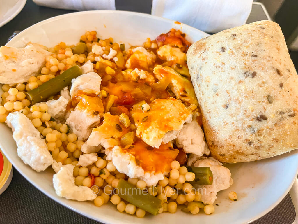 A plate of chicken and pearl pasta with a roll on the side.