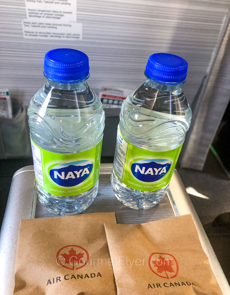 Two bottles of water and two small packages of envelopes with Air Canada's maple leaf logo sit on the armrest of the business class seats.