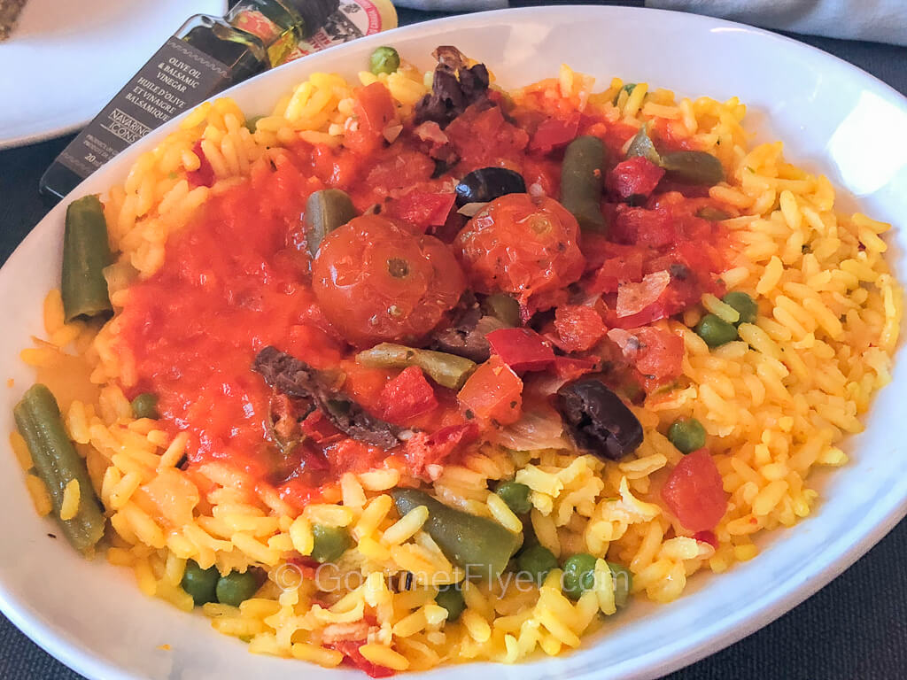 A paella with vegetables is topped with tomato sauce and cherry tomatoes.
