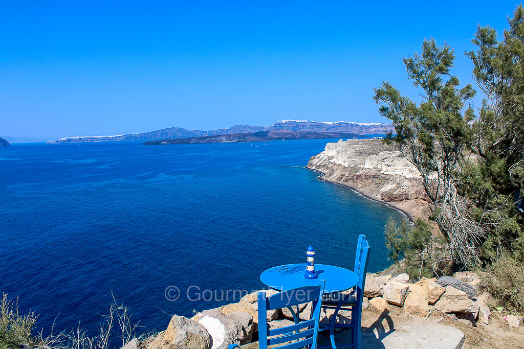 A cute blue round table with two small wooden chairs are placed at the edge of a cliff with great views.