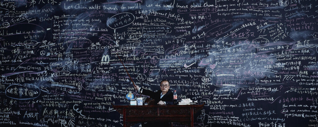A huge blackboard is full of writings in different languages covering various school subjects. The MacDonald's logo and drawing of the Great Wall of China are clearly visible.