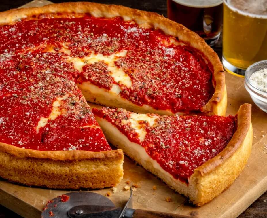 A deep-dish pizza with a tall edge is topped with cheese and tomato sauce.