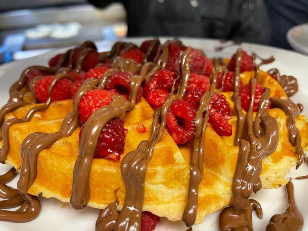 A waffle on a plate is topped with raspberries and Nutella.