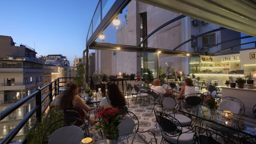 An open-air rooftop restaurant with about a dozen dining tables is shown at dusk.
