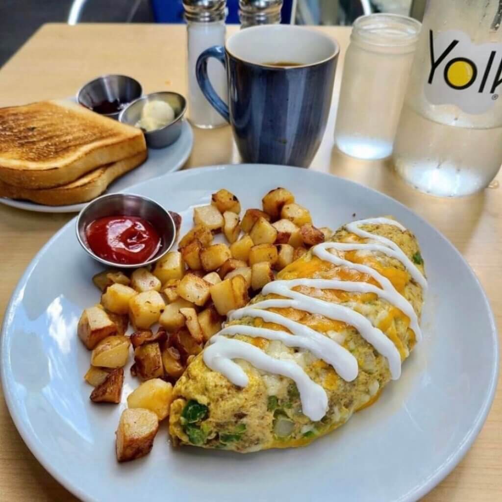 A large omelet is served with fried diced potatoes with ketchup on the side. A side of toast accompanies the order.