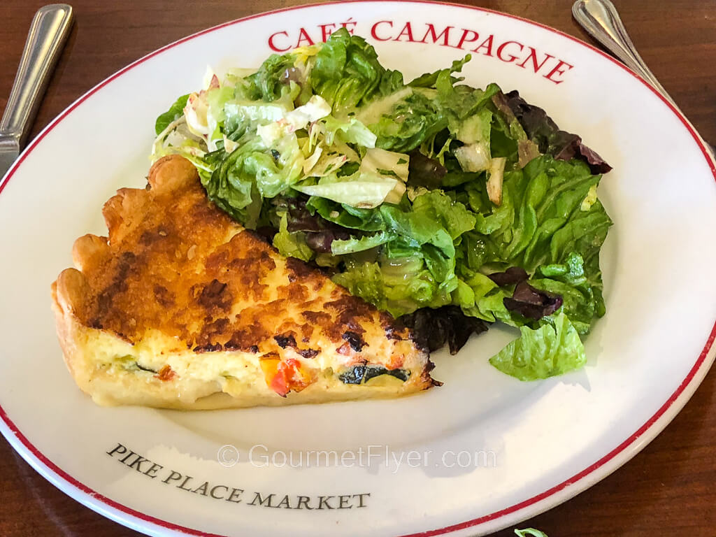 A triangular slice of quiche is served on a plate together with a side of green salad.