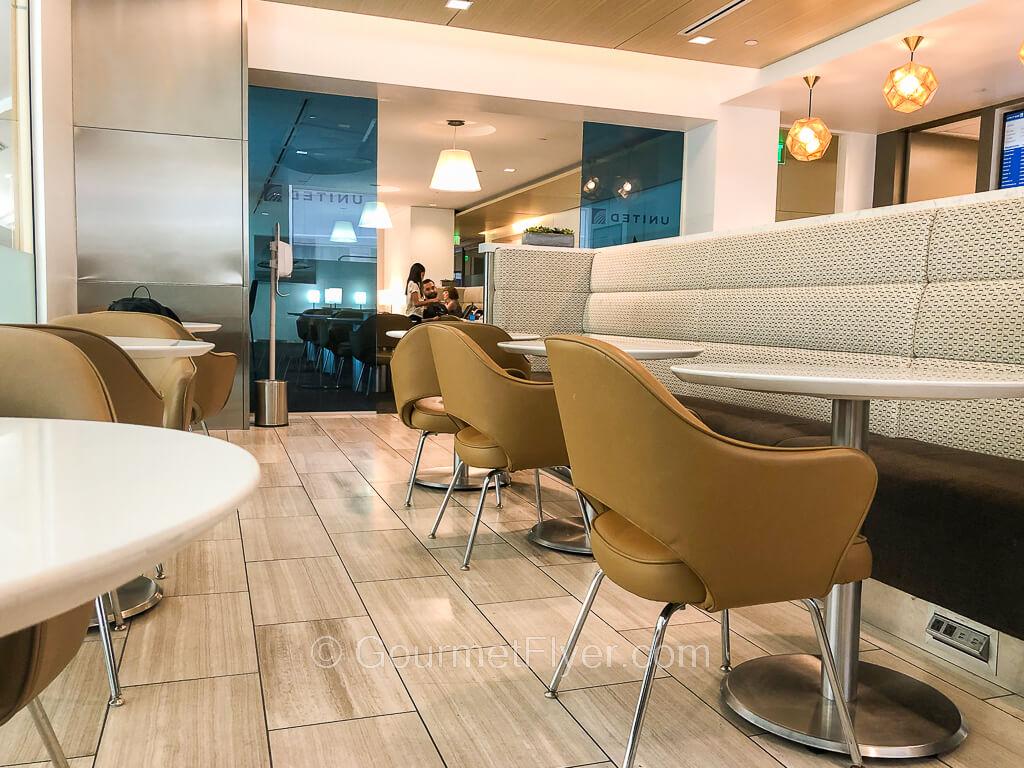 Two rows of round dining tables with chairs are placed behind two blue glass partitions.