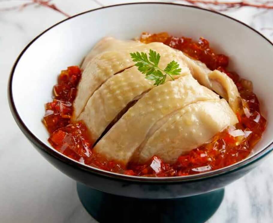 A cut-up steamed chicken sits atop pieces of wine jelly in a bowl.