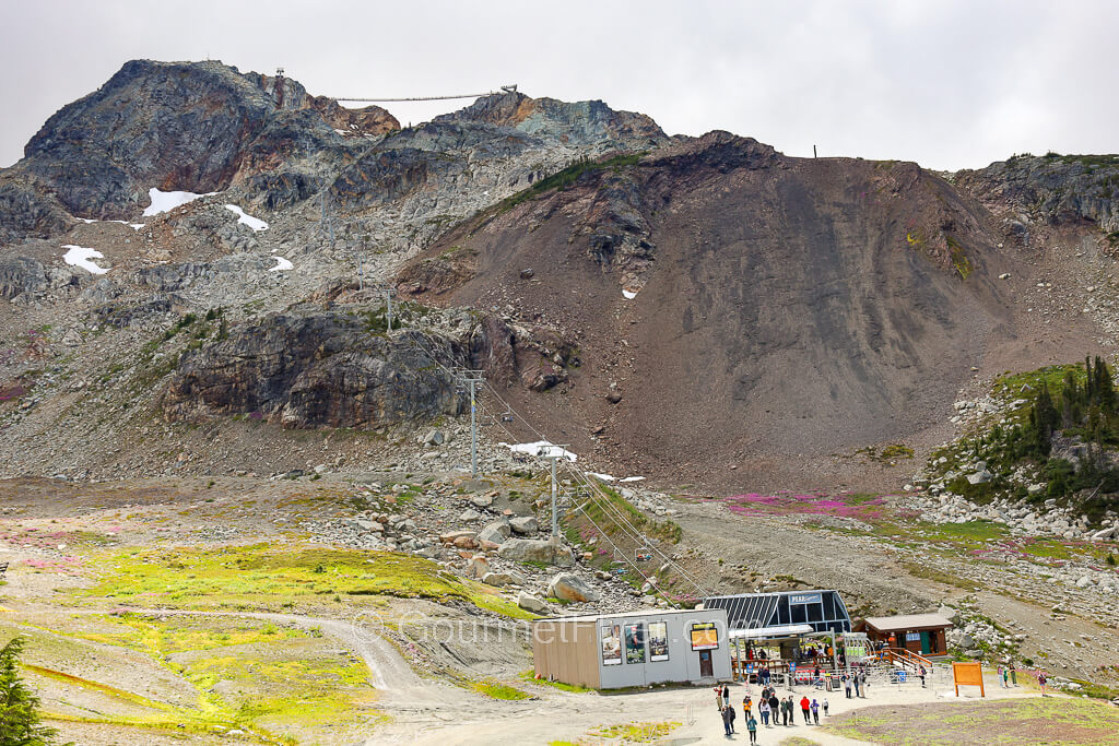 The Cloudraker suspension bridge can be seen from a distance in the background, between two mountain peaks.