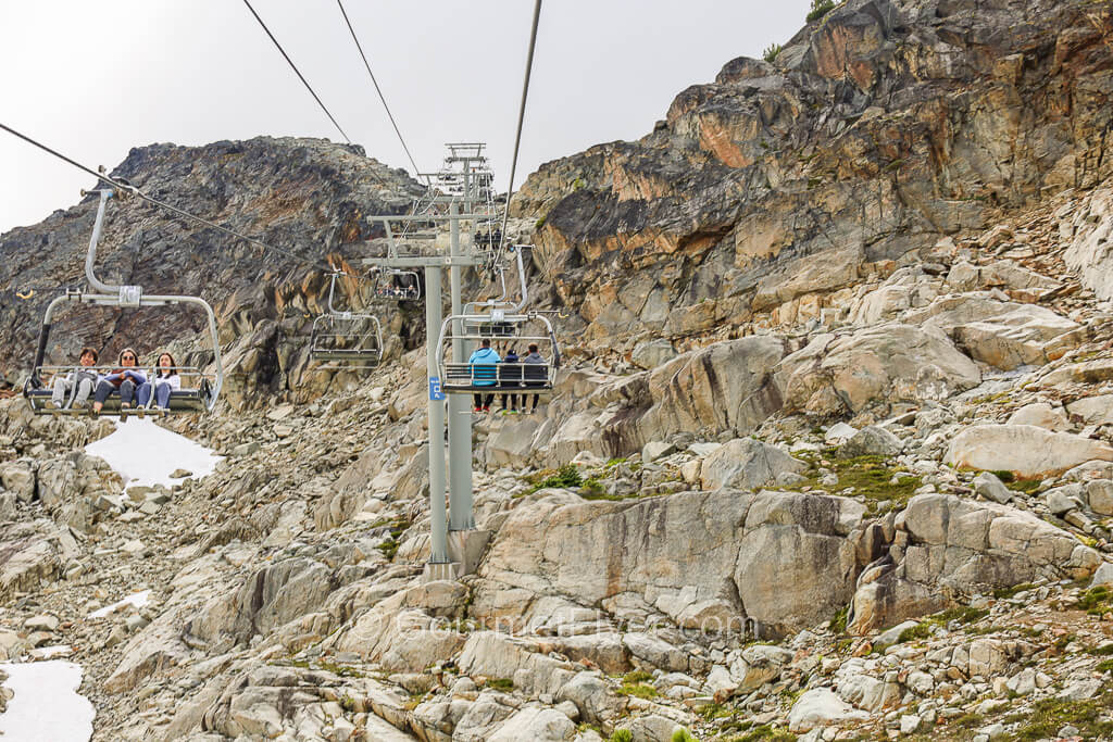 Chairlifts are carrying travelers in both directions across a rocky mountain top.