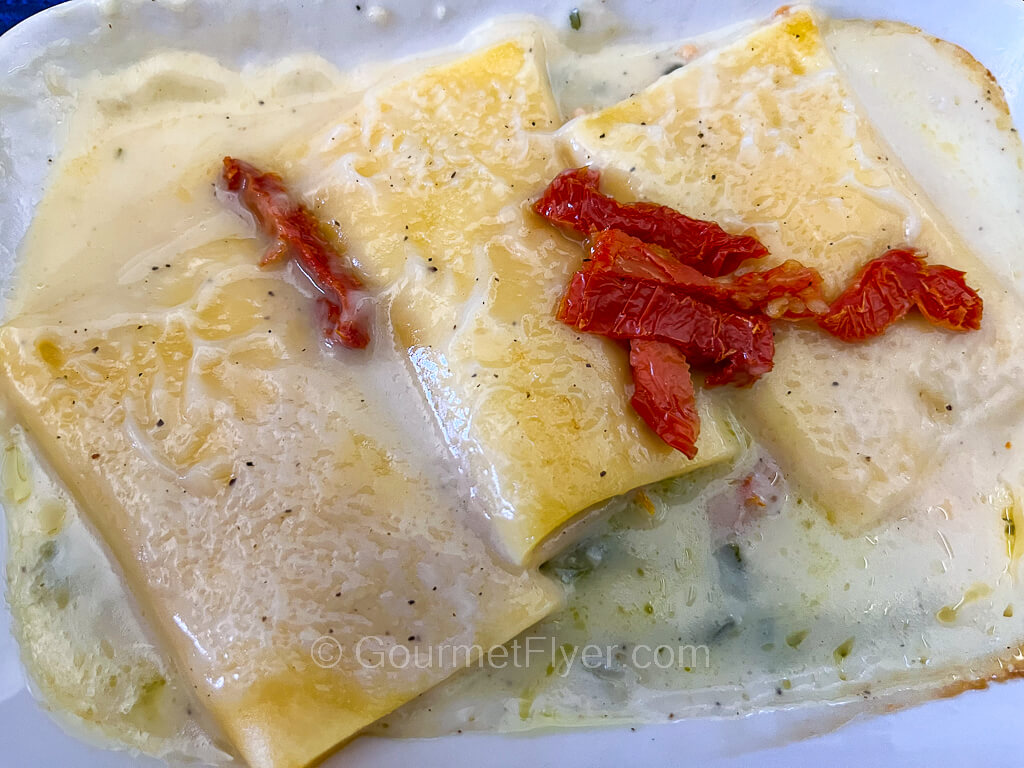A dish of manicotti is served in a white creamy sauce and topped with pieces of sundried tomatoes.